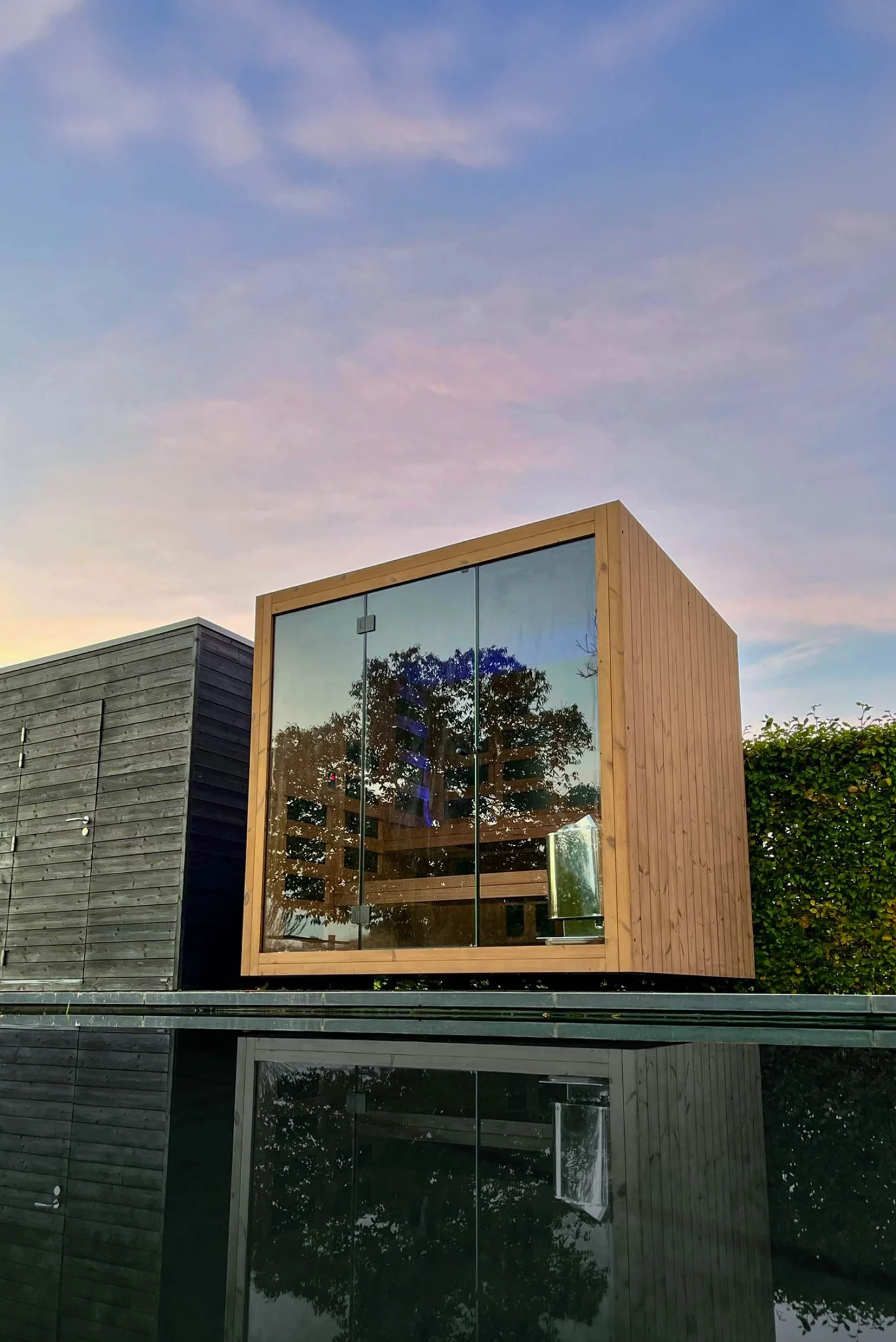 Luxe kubusvormige design buitensauna met infrarood glazen voorwand en moderne thermowood afwerking, in de tuin voor een ultieme outdoor wellness ervaring.