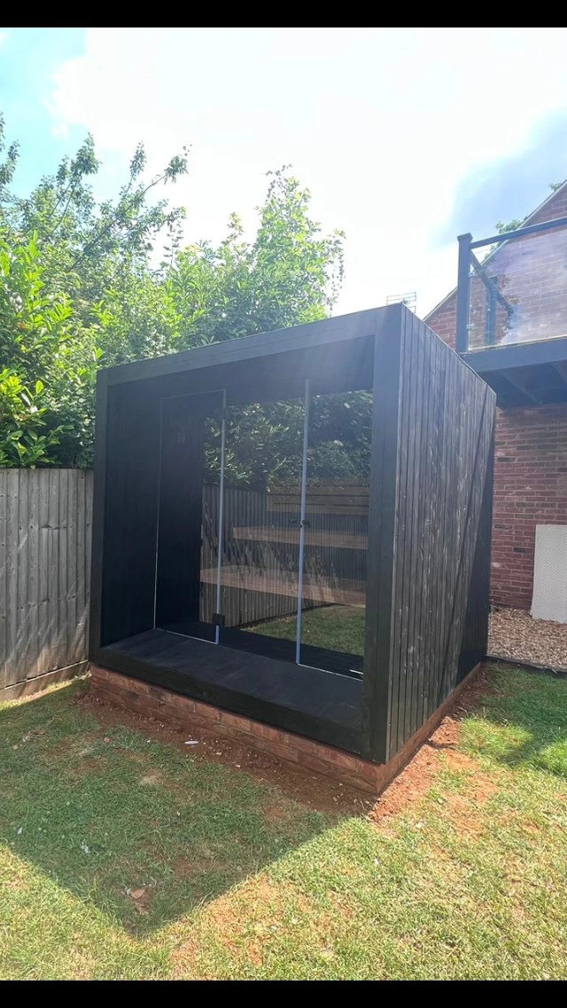 Luxe kubusvormige design buitensauna met infrarood glazen voorwand en moderne thermowood afwerking, in de tuin voor een ultieme outdoor wellness ervaring.