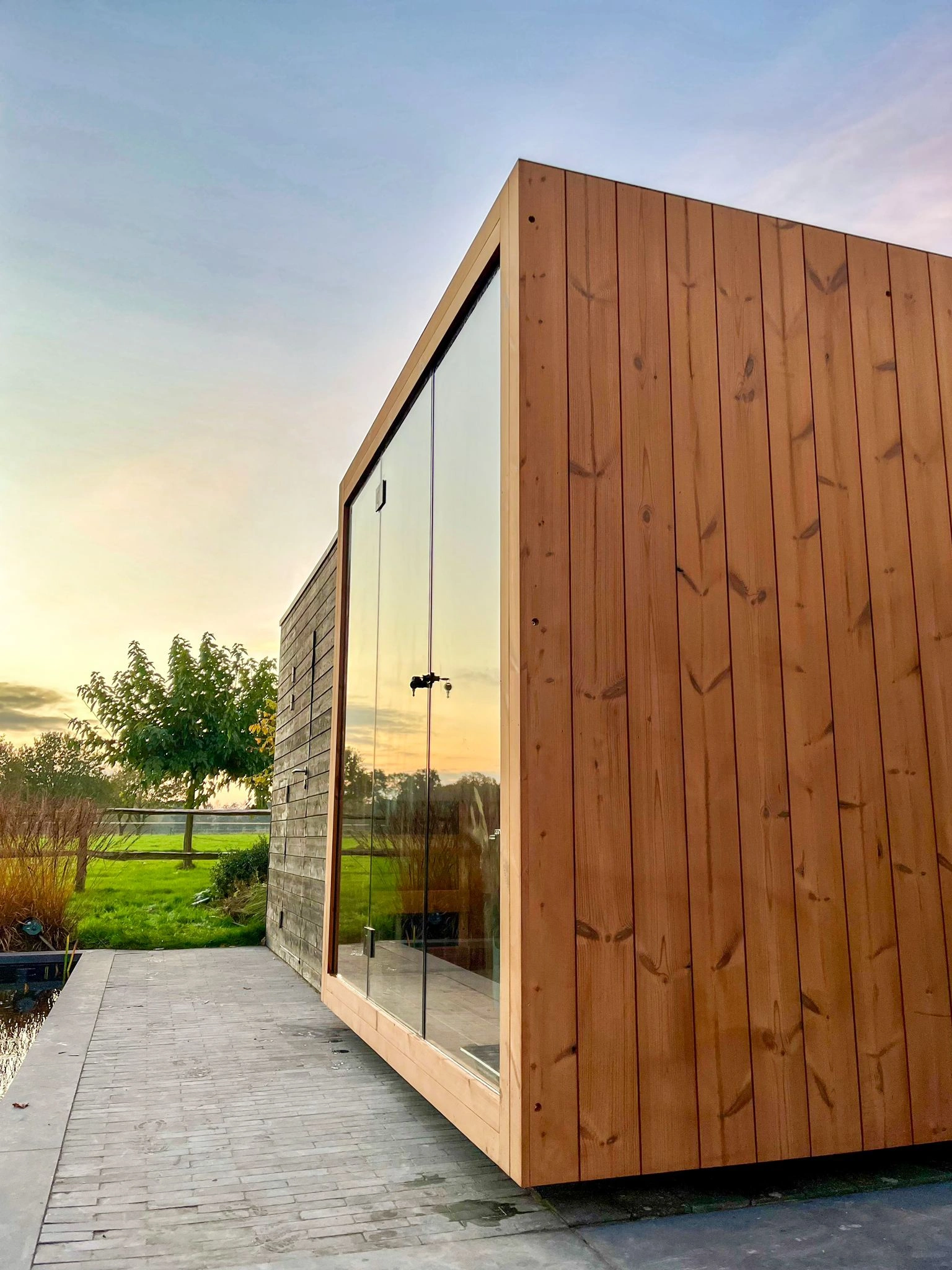 Luxe kubusvormige design buitensauna met infrarood glazen voorwand en moderne thermowood afwerking, in de tuin voor een ultieme outdoor wellness ervaring.