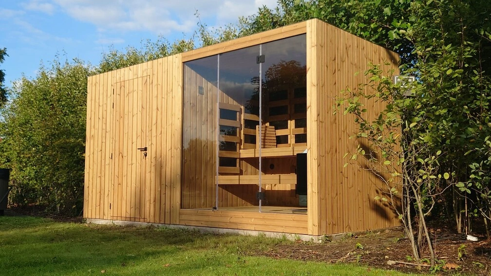 Luxe kubusvormige design buitensauna met infrarood, berging, glazen voorwand en moderne thermowood afwerking, in de tuin voor een ultieme outdoor wellness ervaring.