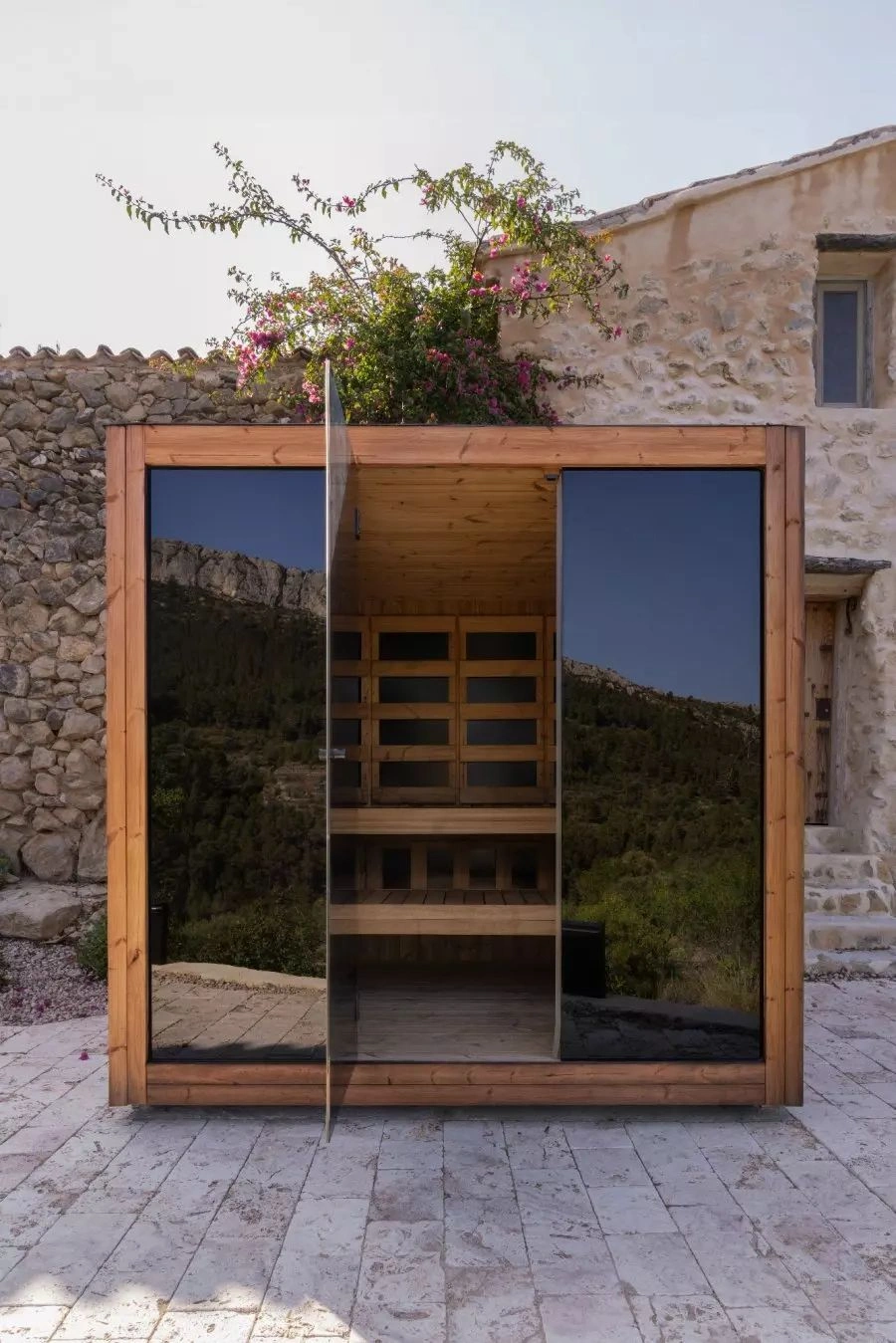 Luxe kubusvormige design buitensauna met infrarood glazen voorwand en moderne thermowood afwerking, in de tuin voor een ultieme outdoor wellness ervaring.