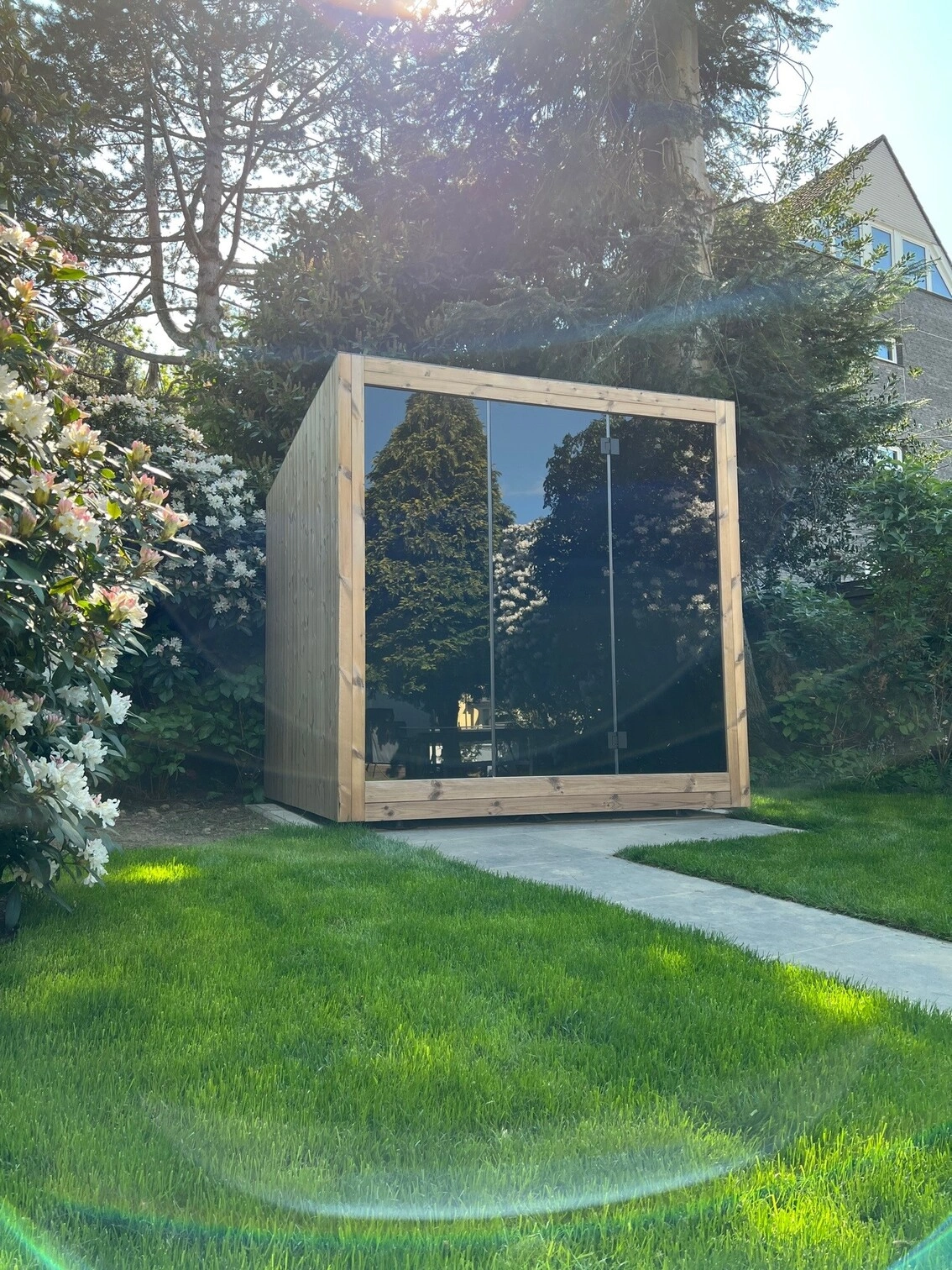 Luxe kubusvormige design buitensauna met infrarood glazen voorwand en moderne thermowood afwerking, in de tuin voor een ultieme outdoor wellness ervaring.