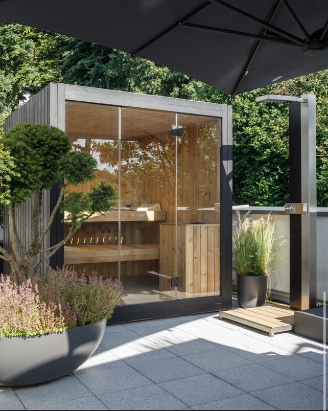 Luxe kubusvormige design buitensauna met glazen voorwand en moderne thermowood afwerking, in de tuin voor een ultieme outdoor wellness ervaring.