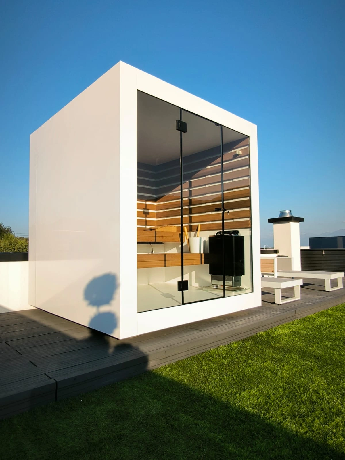 Luxe kubusvormige design buitensauna met glazen voorwand en moderne aluminium afwerking, in de tuin voor een ultieme outdoor wellness ervaring.