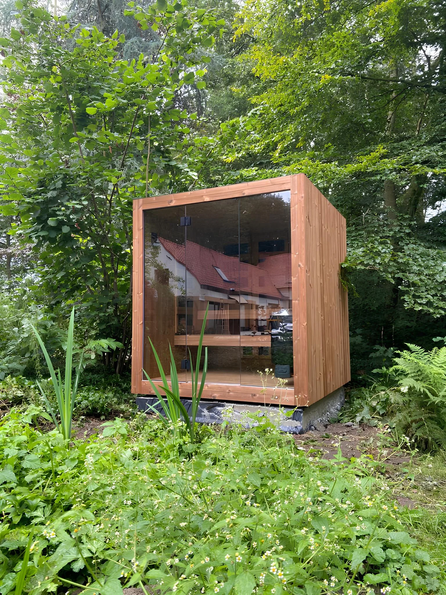 Luxe kubusvormige design buitensauna met glazen voorwand en moderne thermowood afwerking, in de tuin voor een ultieme outdoor wellness ervaring.