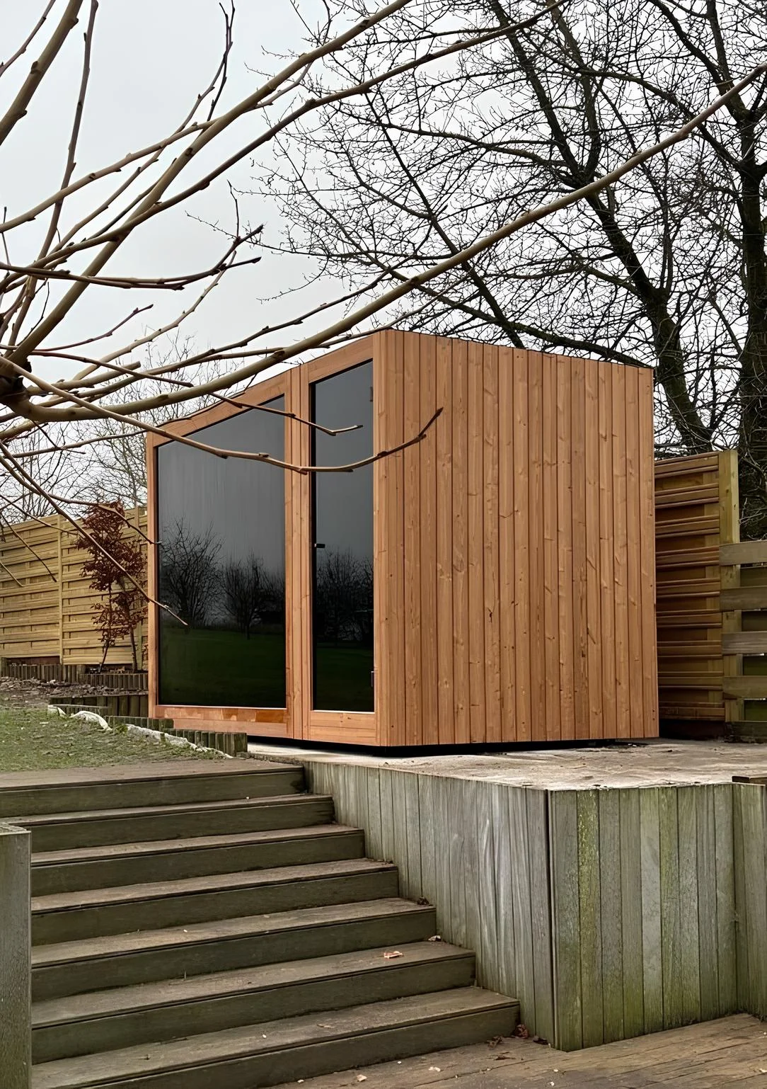 Luxe kubusvormige design buitensauna met douche, glazen voorwand en moderne thermowood afwerking, in de tuin voor een ultieme outdoor wellness ervaring.