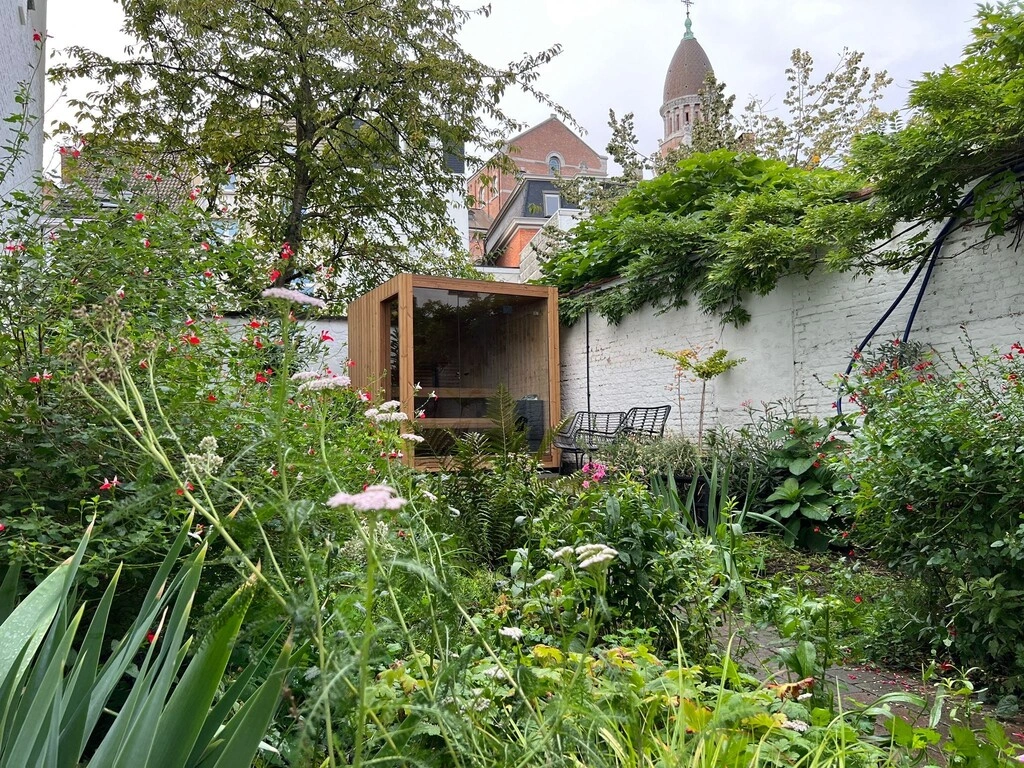 Luxe kubusvormige design buitensauna met glazen voorwand en moderne thermowood afwerking, in de tuin voor een ultieme outdoor wellness ervaring.