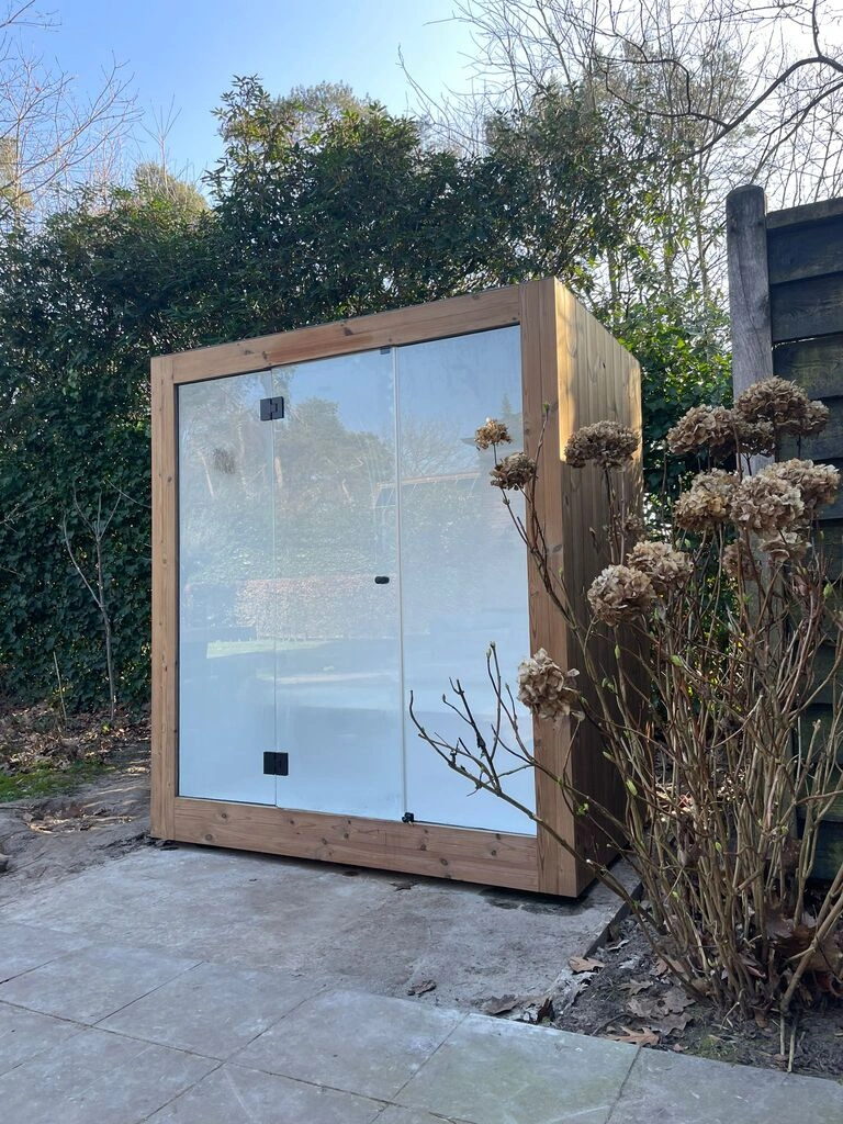 Luxe kubusvormige design buitenstoomcabine met glazen voorwand en moderne thermowood afwerking, in de tuin voor een ultieme outdoor wellness ervaring.
