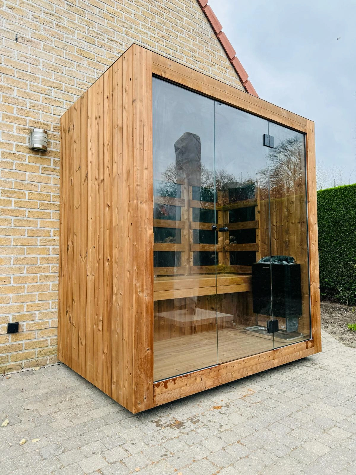 Luxe kubusvormige design buitensauna met infrarood glazen voorwand en moderne thermowood afwerking, in de tuin voor een ultieme outdoor wellness ervaring.