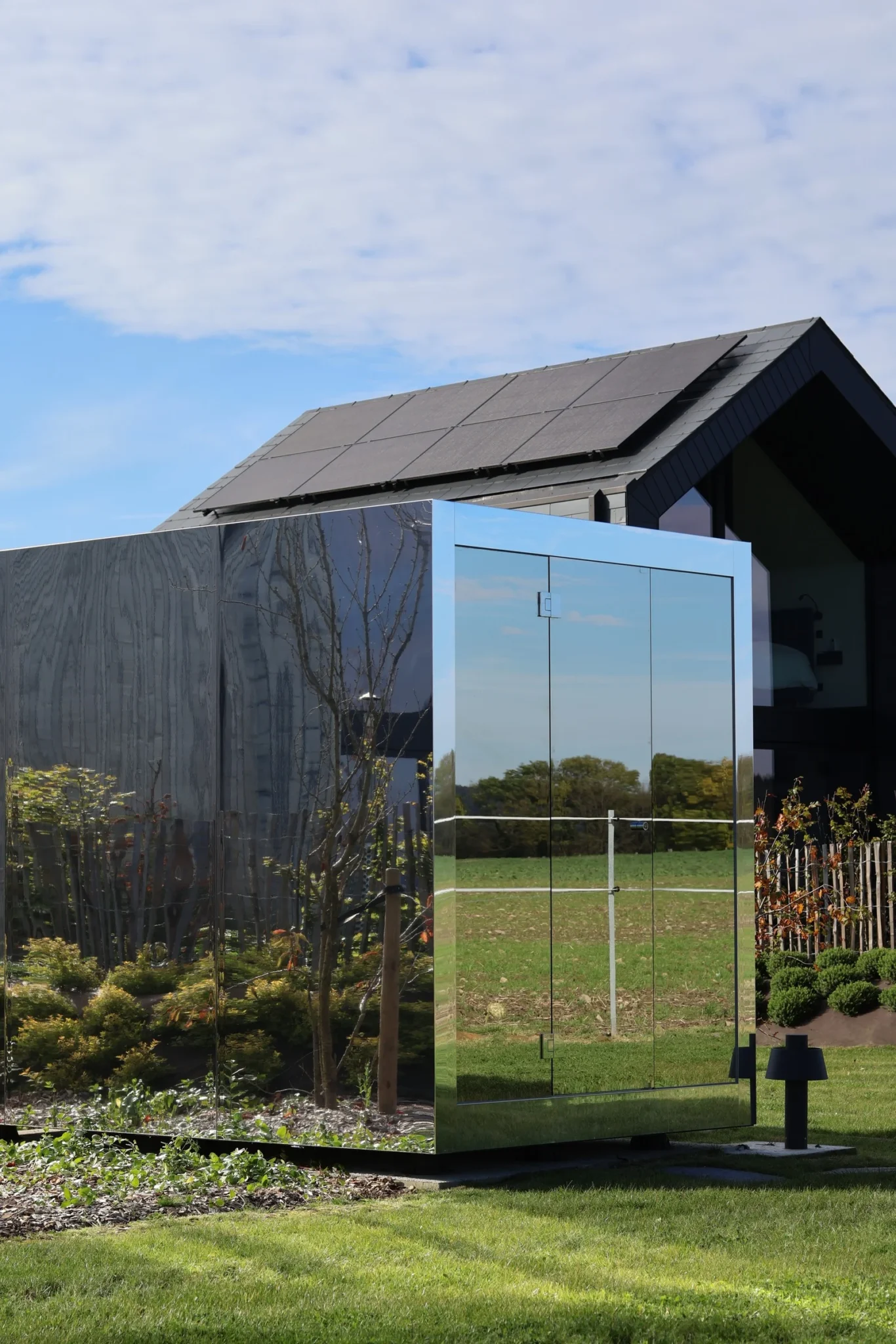 Luxe kubusvormige design buitensauna met moderne spiegelglasafwerking, in de tuin voor een ultieme outdoor wellness ervaring.