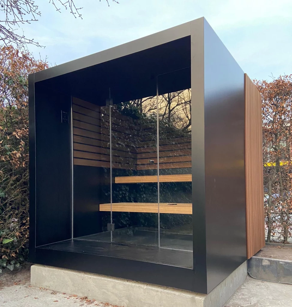Luxe kubusvormige design buitensauna met glazen voorwand en moderne aluminium afwerking, in de tuin voor een ultieme outdoor wellness ervaring.