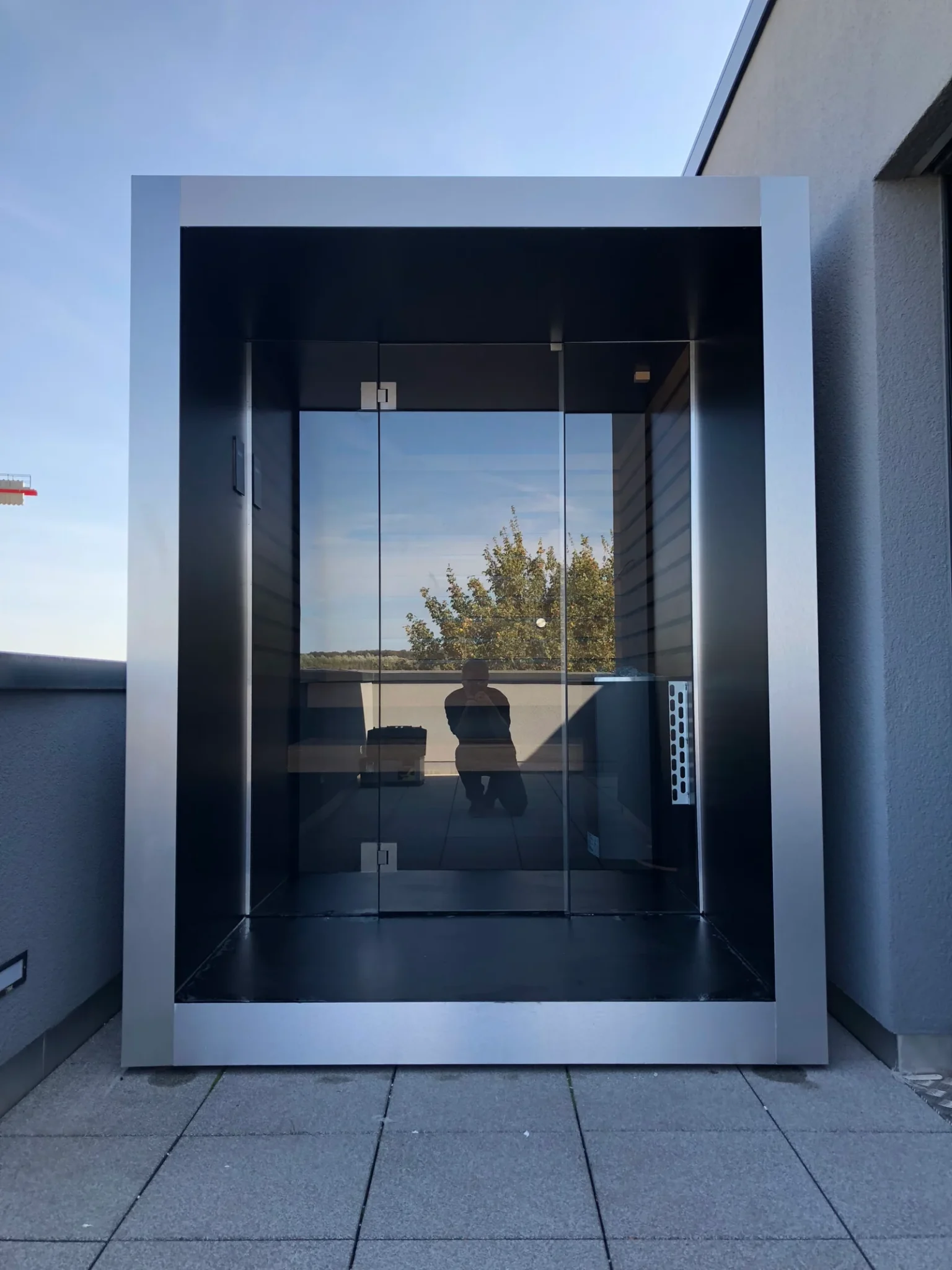 Luxe kubusvormige design compacte buitensauna met infrarood, glazen voorwand en moderne inox afwerking, in de tuin voor een ultieme outdoor wellness ervaring.
