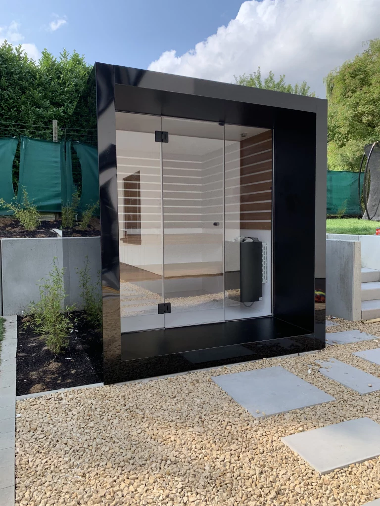 Luxe kubusvormige design buitensauna met glazen voorwand en moderne aluminium afwerking, in de tuin voor een ultieme outdoor wellness ervaring.