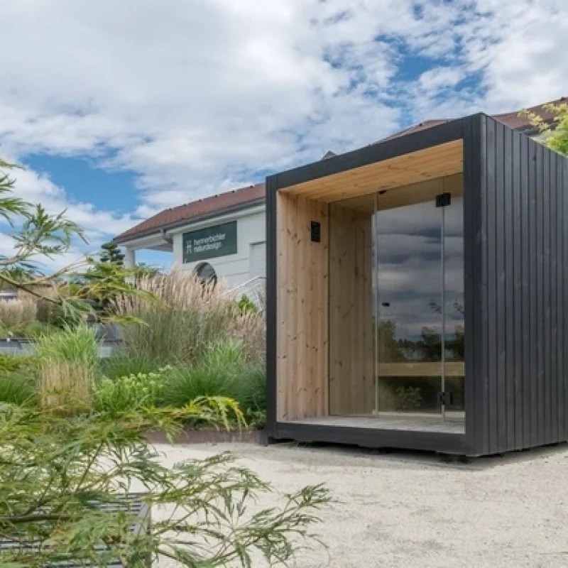 Luxuriöse kubusförmige Design-Außensauna mit Glasfront und moderner Thermoholz-Oberfläche, im Garten für ein ultimatives Outdoor-Wellness-Erlebnis.