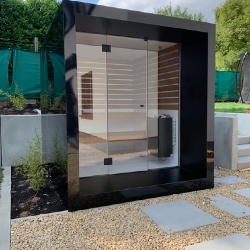 Luxuriöse kubusförmige Design-Außensauna mit Glasfront und moderner Aluminium Oberfläche, im Garten für ein ultimatives Outdoor-Wellness-Erlebnis.