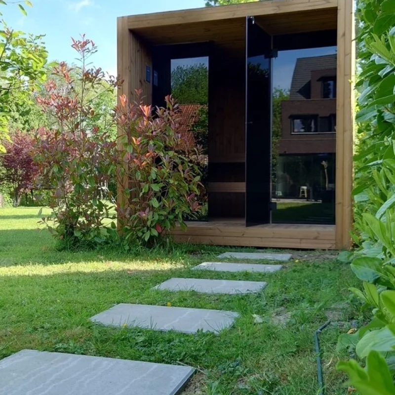 Luxuriöse kubusförmige Design-Außensauna mit Glasfront und moderner Thermoholz-Oberfläche, im Garten für ein ultimatives Outdoor-Wellness-Erlebnis.