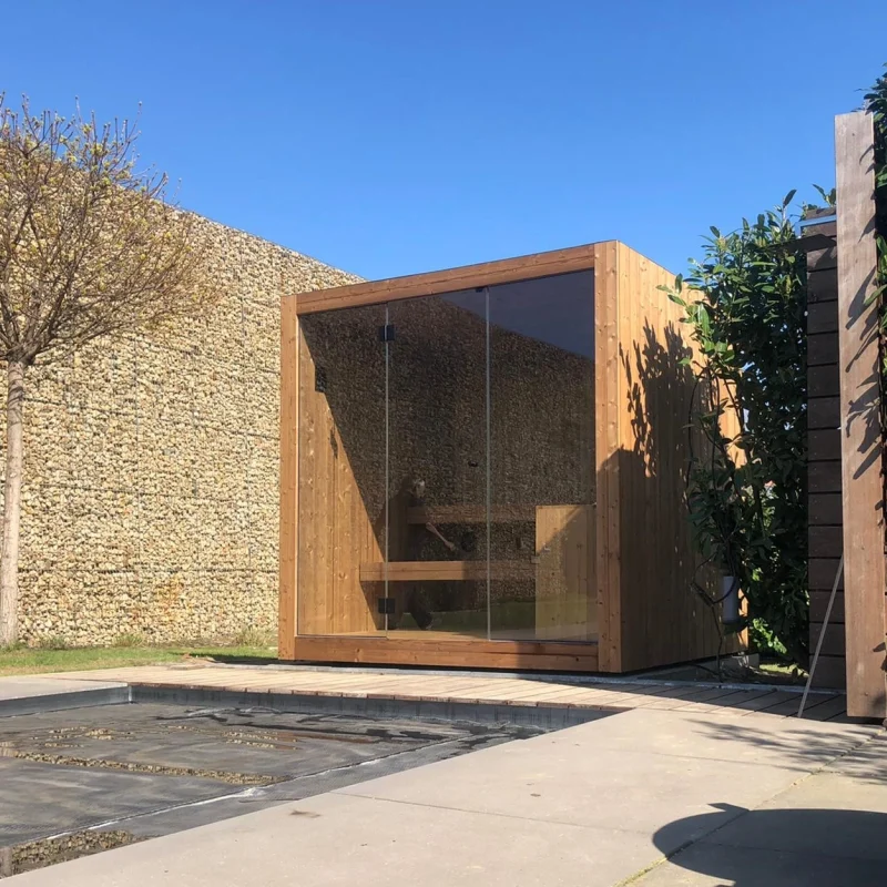 Luxe kubusvormige design buitensauna met glazen voorwand en moderne thermowood afwerking, in de tuin voor een ultieme outdoor wellness ervaring.