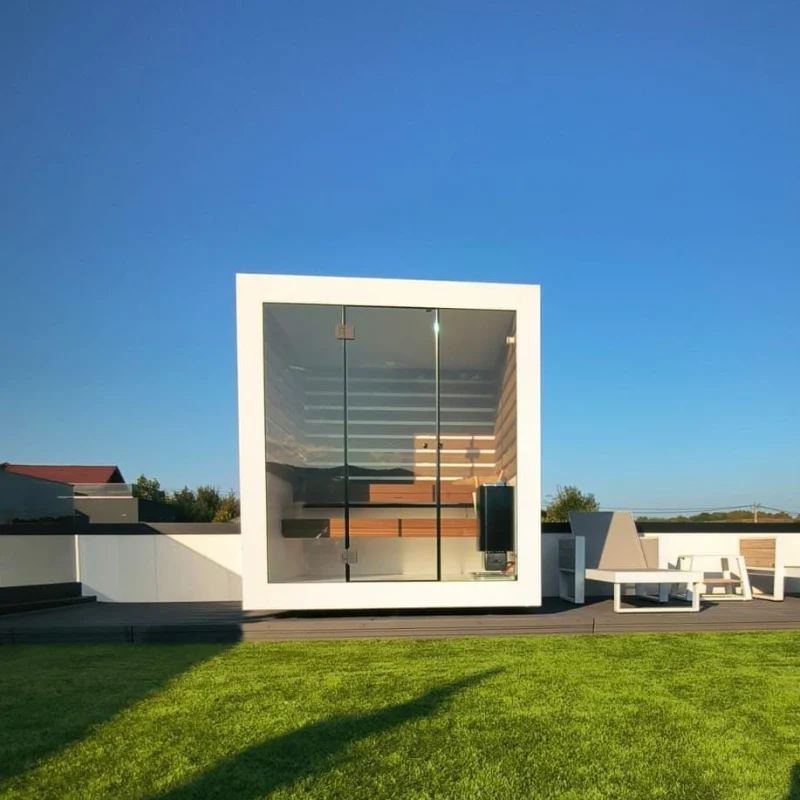 Luxe kubusvormige design buitensauna met glazen voorwand en moderne aluminium afwerking, in de tuin voor een ultieme outdoor wellness ervaring.