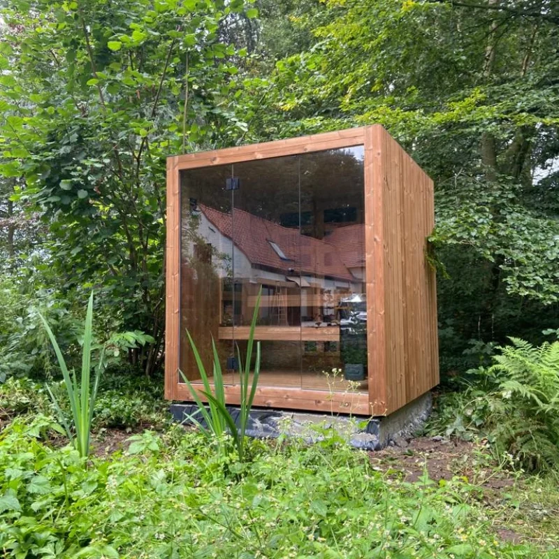 Luxe kubusvormige design buitensauna met glazen voorwand en moderne thermowood afwerking, in de tuin voor een ultieme outdoor wellness ervaring.