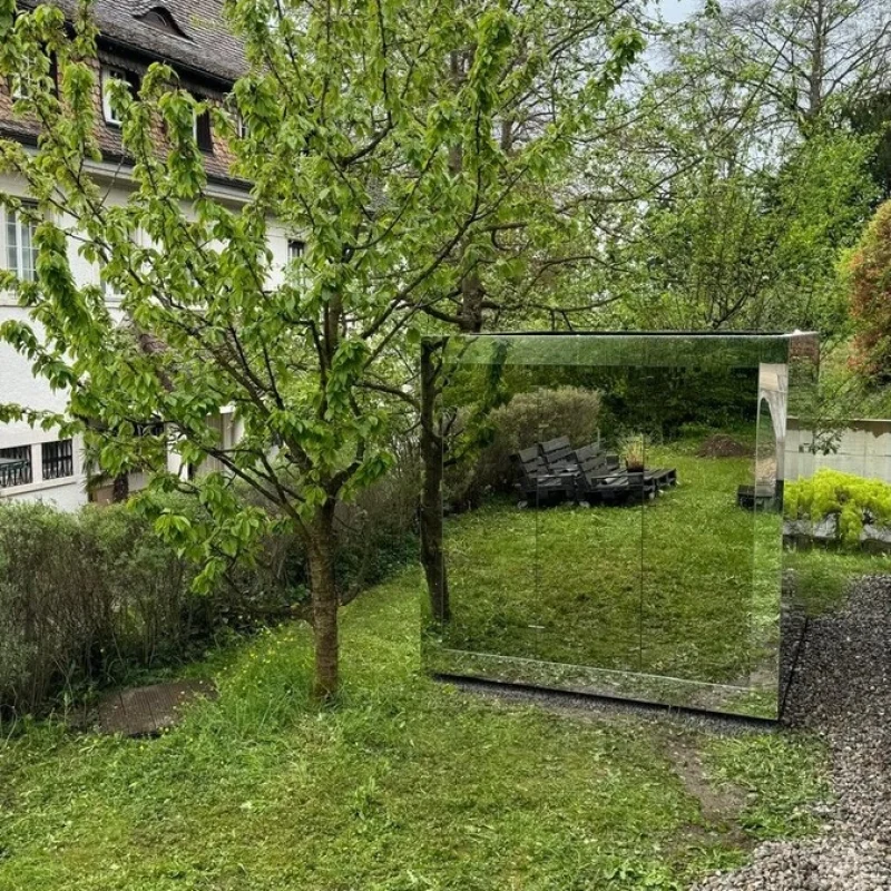 Sauna extérieur de luxe en forme de cube avec finition en verre miroir moderne, dans le jardin pour une expérience de bien-être en plein air ultime.