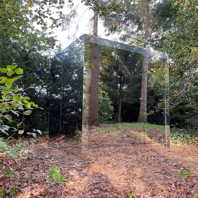 Sauna extérieur de luxe en forme de cube avec finition en verre miroir moderne, dans le jardin pour une expérience de bien-être en plein air ultime.