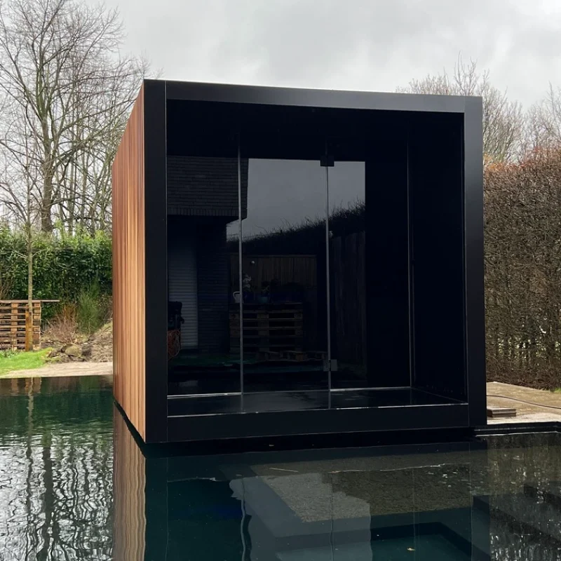 Sauna extérieur de luxe en forme de cube avec façade en verre et finition moderne en aluminium, dans le jardin pour une expérience de bien-être en plein air ultime.