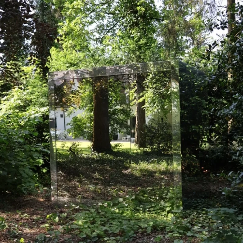 Sauna extérieur de luxe en forme de cube avec finition en verre miroir moderne, dans le jardin pour une expérience de bien-être en plein air ultime.